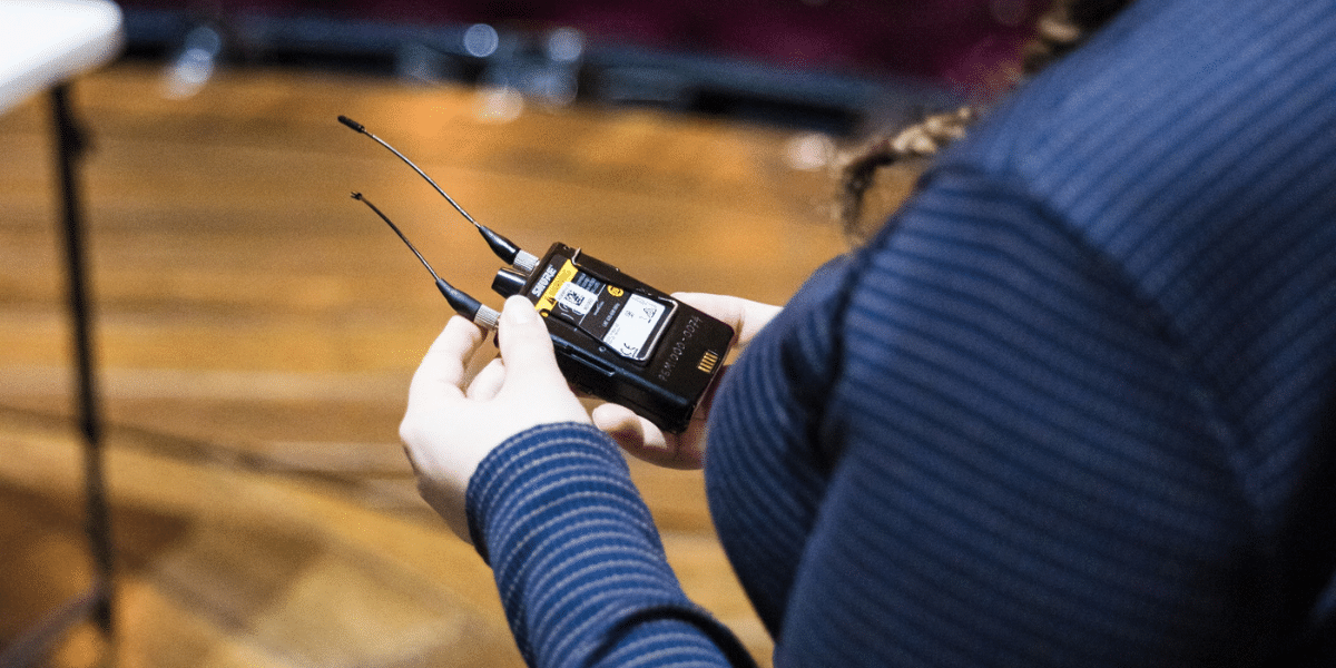 Person holding two wireless microphone transmitters backstage.