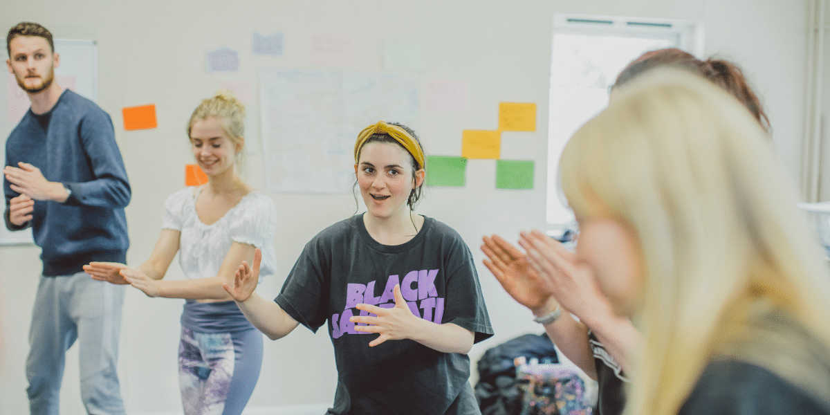 A group of people participate in an interactive workshop, engaged in movement and expression in a bright, open space.