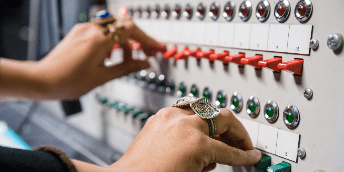 Close-up of hands adjusting red and green switches on an industrial control panel.