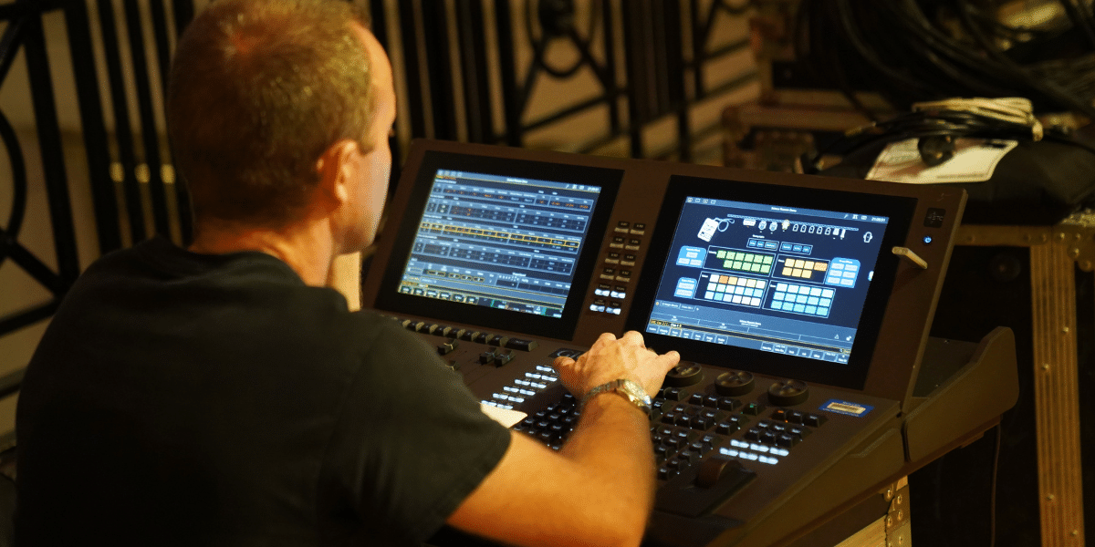 A lighting technician adjusts settings on a complex mixing console during a live event, focused on digital controls and displays.