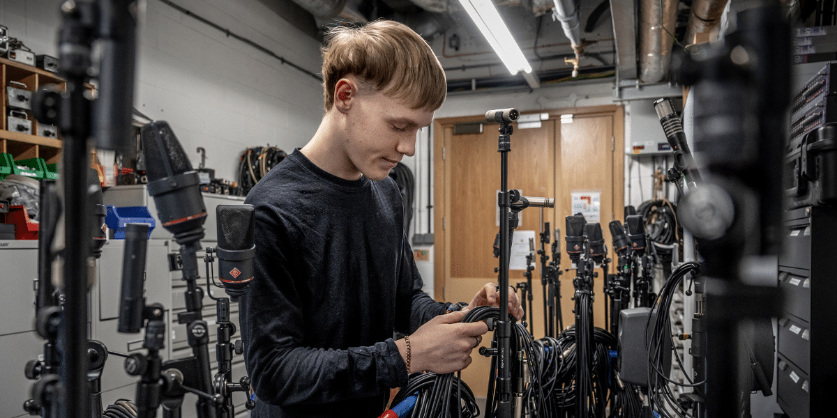 Person in a black shirt handling equipment amidst many tripods and cables.